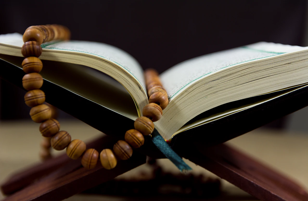An open Quran on a wooden stand with prayer beads